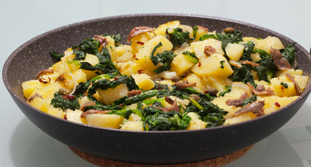 Potatoes with anchovies and spinach in a frying pan close-up.の写真素材