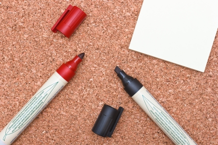 red and black markers with white sticky note on cork backgroundの写真素材