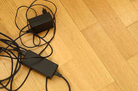 Electric plug, transformer and cables on the parquet floor.