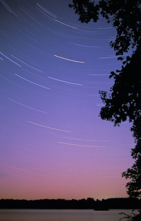 Long exposure star trails, rotating around the North Star. Aurora Borealis glowing green and red...