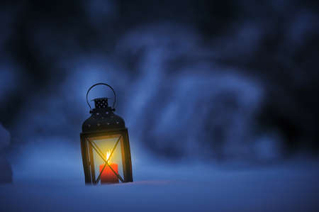 Candle lantern in snow against defocused bokeh backgroundの写真素材