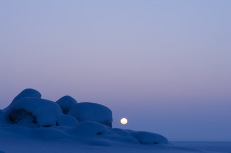 Winter landscape at dusk. Sun setting behind snow covered boulders.の写真素材