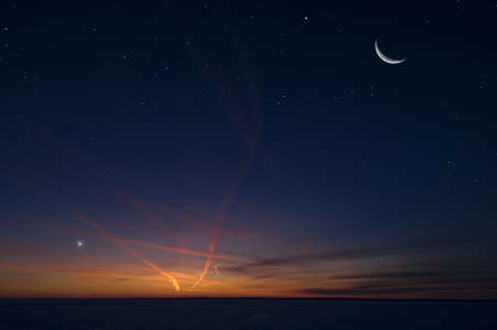 Night sky with stars, crescent Moon, planet Venus and airplane vapour trails.の写真素材