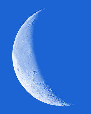 Waning Crescent Moon with crater detail on blue sky.の写真素材