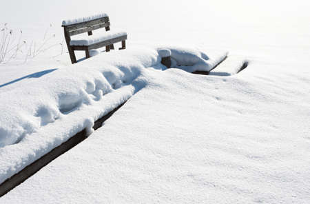 Wooden pier and bench covered with fresh snow.