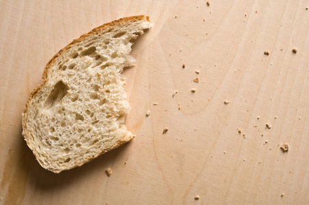 Half eaten slice of bread on wooden table.