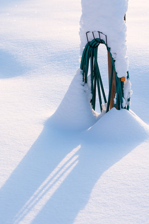 Coiled water hose buried in fresh newly fallen powder snow, winter in the garden.の写真素材