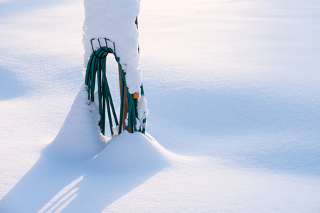 Coiled water hose buried in fresh newly fallen snow, winter in the garden.の写真素材