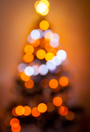 Defocused blurry christmas tree silhouette with blurred lights on warm background. Christmas concept.の写真素材