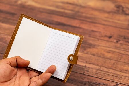 Blank notepad open in hand with wooden wallpaper back