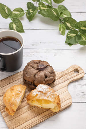 Two types of cream puffs and coffee cups on the cutting boardの写真素材