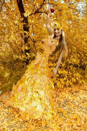 Two girls, in dresses from leaves, having joined hands, walk on a footpath in autumn woodの写真素材