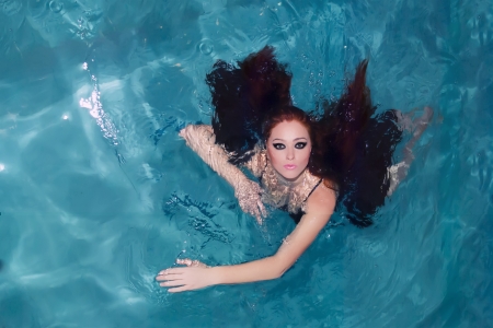Fashionable and beautiful, young girl model with long hair, dressed in colorful flowing fabrics, swimming in the blue water の写真素材