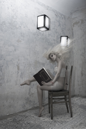 A beautiful girl with long hair in a mysterious and gloomy room, sitting on an old chair, reading a book surrounded by the order of paper lanterns in the air.の写真素材