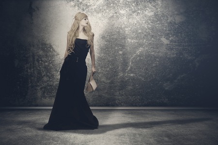 Mysterious woman with long locks in a black gothic dress, standing in the dark and empty roomの写真素材