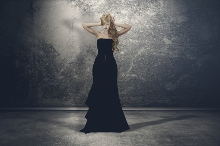 Mysterious woman with long locks in a black gothic dress, standing in the dark and empty roomの写真素材