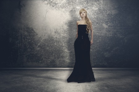 Mysterious woman with long locks in a black gothic dress, standing in the dark and empty roomの写真素材