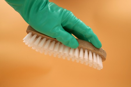 Hand with a green rubber glove holding a brush isolated on orange backgroundの写真素材