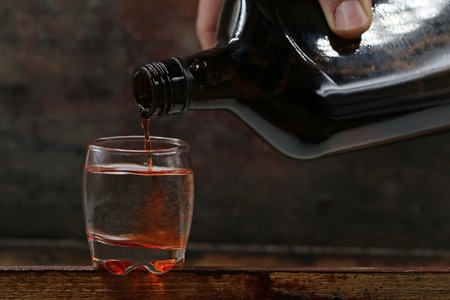 rum is poured from bottle into a shot glass, served on dark wooden backgroundの写真素材