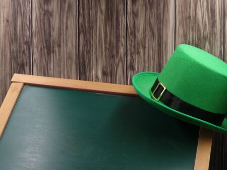 green hat on blackboard and wooden background with copy space, st. patricks day concept.の写真素材