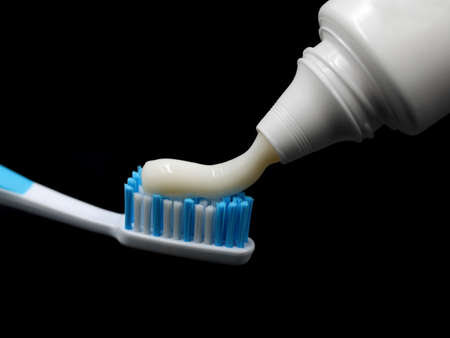 Toothpaste is squeezed out of the tube onto a blue toothbrush, isolated on black backgroundの写真素材
