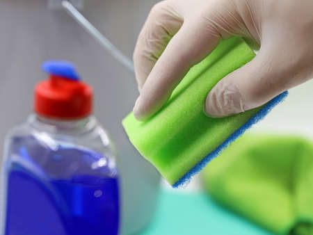 hand in gloves holds sponge over domestic utensils, concept background of household cleaning, close...