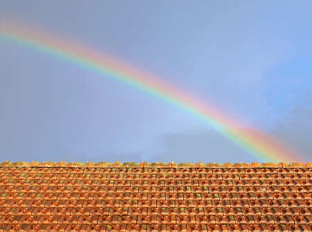 rainbow over the rooftop of an old house with rainy weather clouds on skyの写真素材