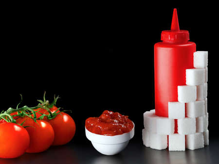 fresh tomatoes with a serving of ketchup and a red ketchup bottle with sugar cubes arround on black...
