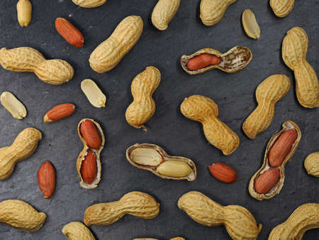 top view of roasted peanuts with and without shell on black slate stone table