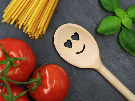 top view of kitchen wooden spoon with smile and heart on slate plate with ingredients for pasta and...