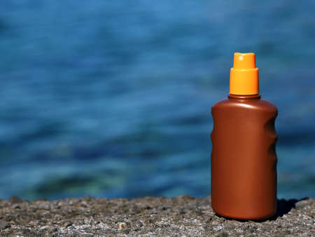 Sunscreen spray bottle on the stone shore with blue sea water background with copy spaceの写真素材