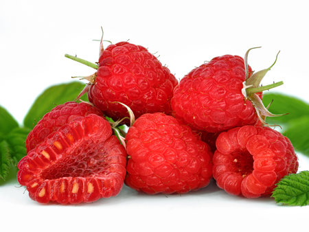 close up of fresh natrual raspberries with halved fruit between green leaves isolated on white...