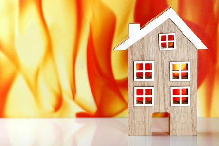wooden model house in front of a fire flames background with copy space, concept image of fire safety or fire protection insuranceの写真素材