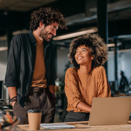 smiling african american businesswoman looking at colleague with laptop in officeの素材