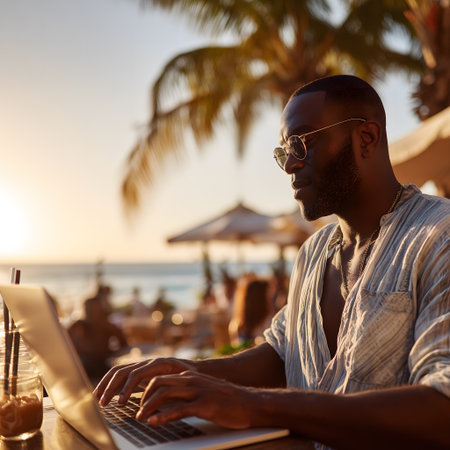 Young african american man working on laptop on the beach at sunsetの素材