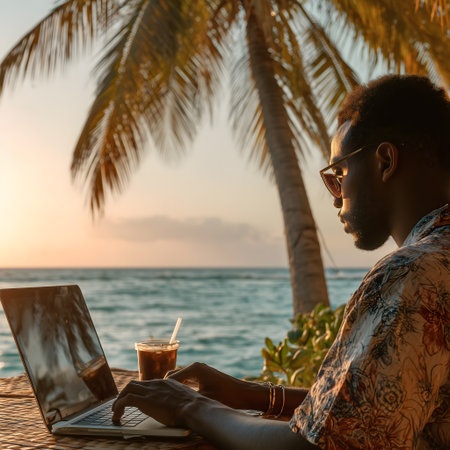 Side view of african american man working with laptop on the beach at sunsetの素材