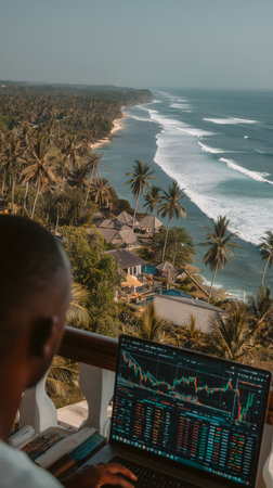 African american trader analyzing stock market on laptop at beach in morningの素材