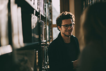 Smiling young man in eyeglasses standing in library and looking at cameraの素材