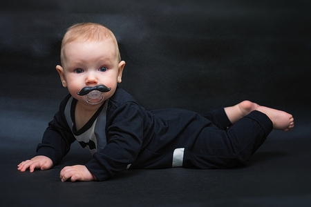 Toddler with pacifier is lying on plaid mustacheの写真素材