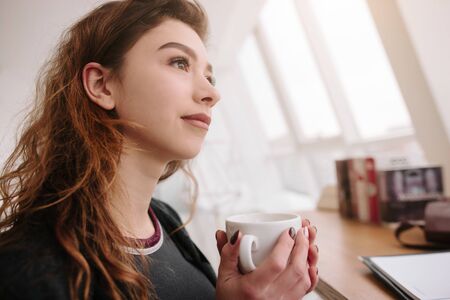Girl her hand holds a cup of coffee, tea and looks straightの写真素材
