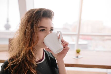 In a cafe, a girl drinks coffee and looks straightの写真素材