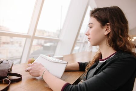 A girl sitting in a cafe, looking out the windowの写真素材