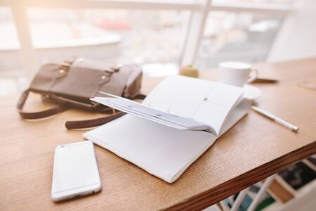 On the table is a phone, a notebook, a bag, a pen and a cup of coffee.