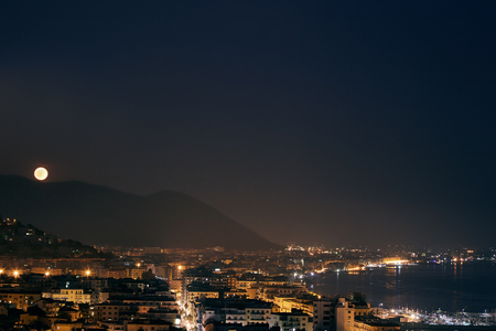 The night panorama of Italian city Salerno. The moon rising from behind the mountains over.の写真素材