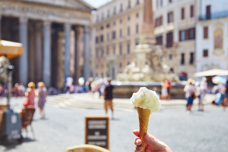 Crop hand holding cone with delectable ice cream on blurred background of square near Pantheon in Rome, Italyの写真素材