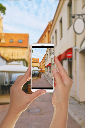 A tourist is taking a photo of empty european street with cafe in the old town in Vilnius on a mobile phoneの写真素材