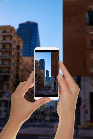 A tourist is taking a photo of the Milan skyscrapers from the next street in the evening without people on a mobile phoneの写真素材