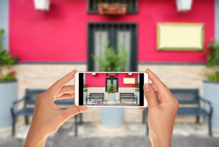 A tourist is taking a photo of two empty benches near the beautiful facade of a cafe painted in pink on one of the Italian streets on a mobile phoneの写真素材