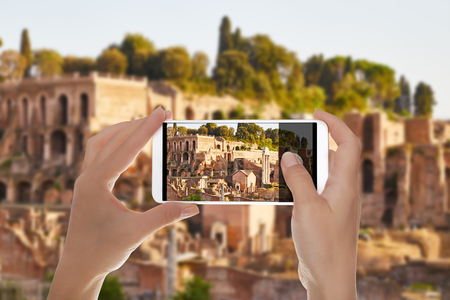 A man is making a photo of the ruins of the Roman Forum without people lit by the evening sun on a mobile phoneの写真素材
