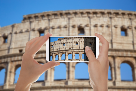 A man is making a photo of the Colosseum against a blue sky Rome, Italy on a mobile phoneの写真素材